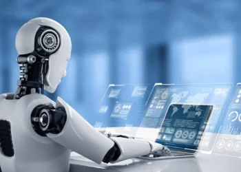A humanoid robot with a sleek design sits at a desk, interacting with a futuristic, transparent digital interface. Multiple holographic screens display various data, charts, and world maps against a blurred blue background, highlighting AI companies to invest in within this high-tech environment. | LESSINVEST