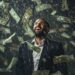 A jubilant man in a dark suit looks upwards with a wide smile as numerous dollar bills rain down around him, celebrating his newfound wealth. The background is dark, highlighting the falling money and creating a dramatic atmosphere, embodying the excitement of discovering the best way to invest $100k. | LESSINVEST