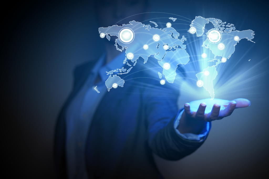 A businessperson holds out a hand with a holographic world map hovering above it. The map features glowing points and lines, representing connectivity across the globe. The background is a deep blue, creating a futuristic and digital feel. | LESSINVEST