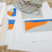 A desk with financial graphs, a pencil, calculator, stack of hundred-dollar bills, and a blue notebook on a wooden surface—ideal for building a recession-proof portfolio. The charts show data from 2013 to 2019. | LESSINVEST
