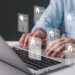 A person types on a laptop keyboard as semi-transparent real estate document icons, featuring house symbols and text, float above—highlighting the digital power of Mortgage Marketing Software. | LESSINVEST