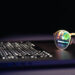 A pair of eyeglasses rests on a laptop keyboard. Computer code and a green Web3 symbol are reflected in the lenses, suggesting programming or cybersecurity work. The background is dark and out of focus. | LESSINVEST