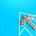 Wooden blocks with human icons are arranged inside a white arrow outline pointing left on a bright blue background, symbolizing teamwork, organizational direction, and effective employee engagement strategies. | LESSINVEST
