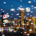 A city skyline at night with illuminated buildings, overlaid with social media notification icons above skyscrapers and along the river—yet in real estate outreach, Neighborhood Letters can outperform digital campaigns for true connectivity. | LESSINVEST