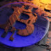 A close-up of a metallic Bitcoin symbol embedded in a digital circuit board, with blue and orange lighting reflecting on the surface, representing cryptocurrency, blockchain technology, and exploring how casino Bitcoins work. | LESSINVEST