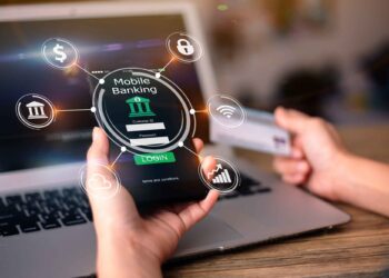 Person using mobile banking app on phone, holding credit card near laptop, with digital banking icons overlaid.